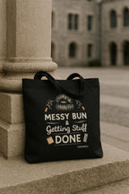 Black tote bag with graphic design and text on a stone surface with a building in the background